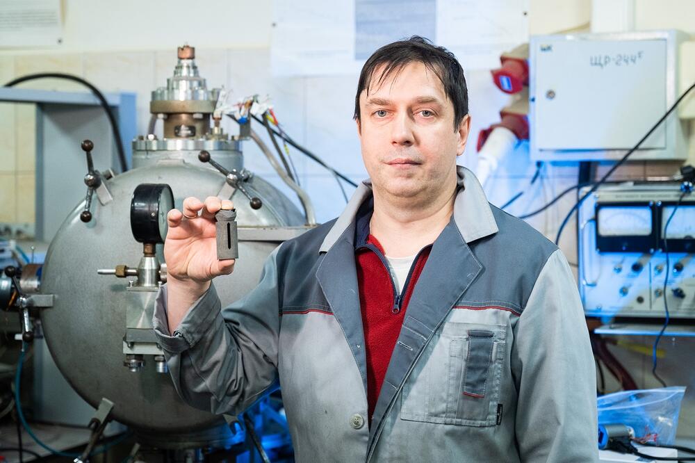 Сергей Жевненко держит в руках вольфрамовый нагреватель на фоне лабораторного оборудования